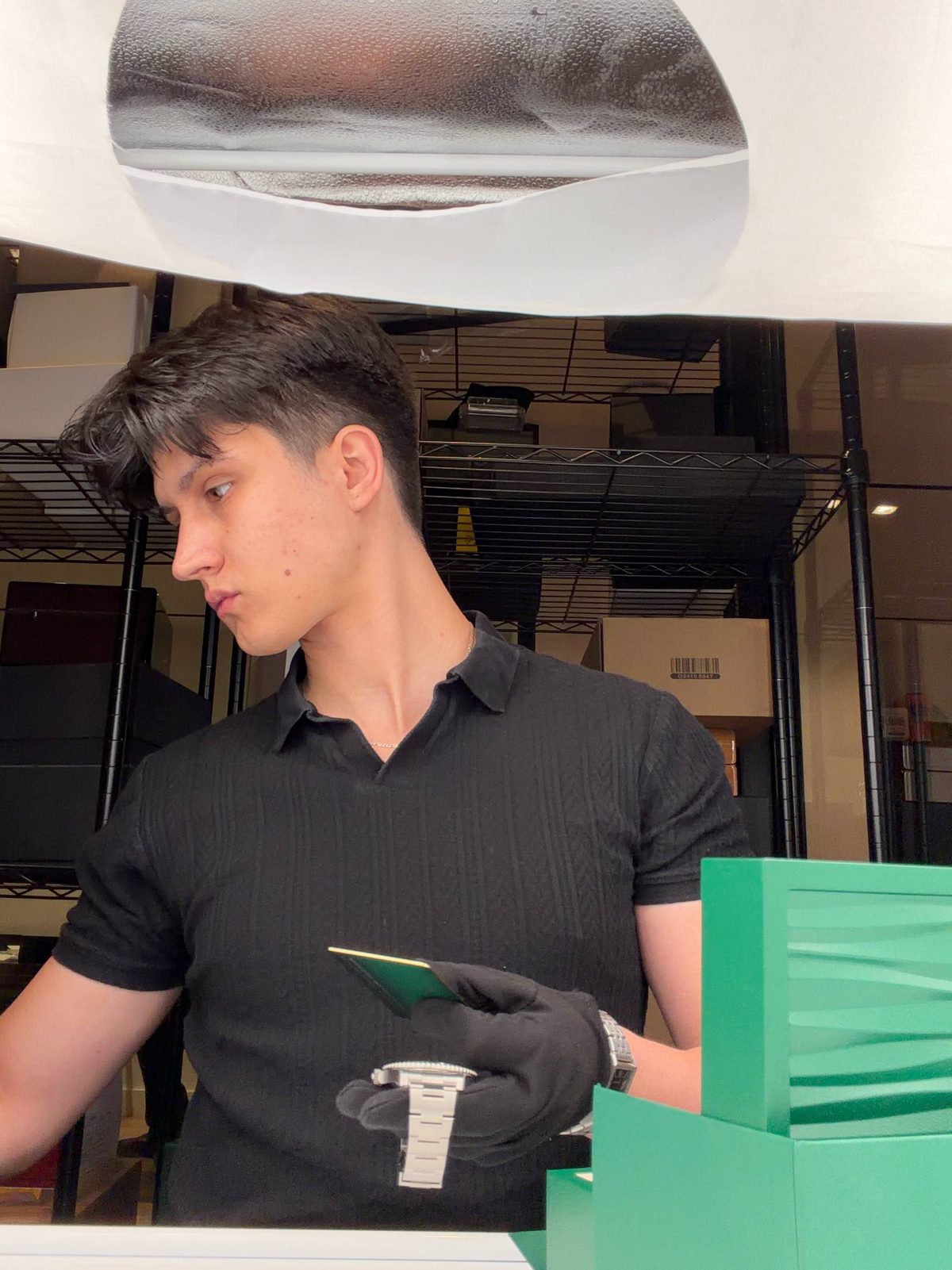 Crew member in black gloves holding a watch and a card beside a green box