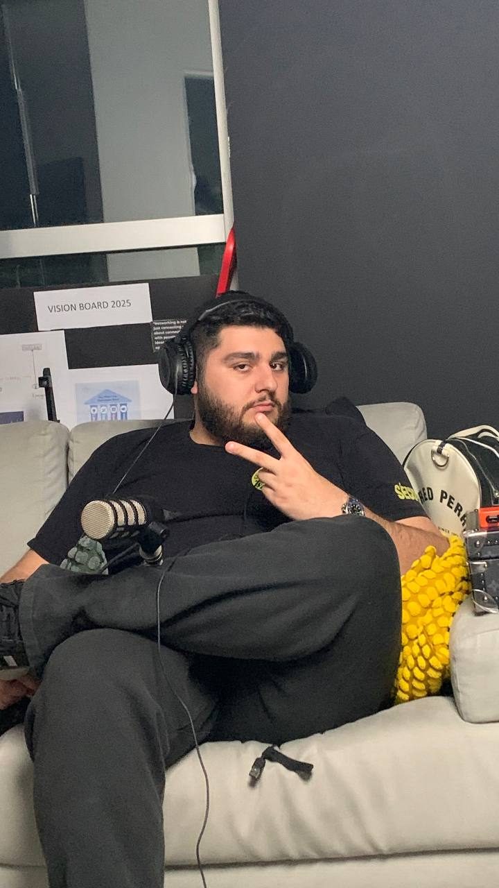 Presenter wearing headphones seated on a sofa beside a microphone